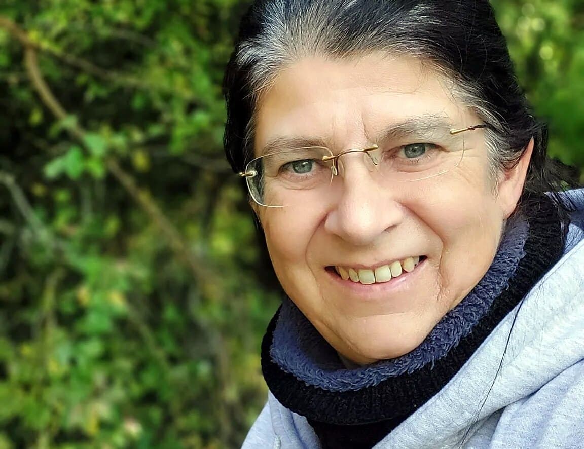 Eva Barwig lächelnd in grauer Kapuzenjacke, dahinter grünes Laub